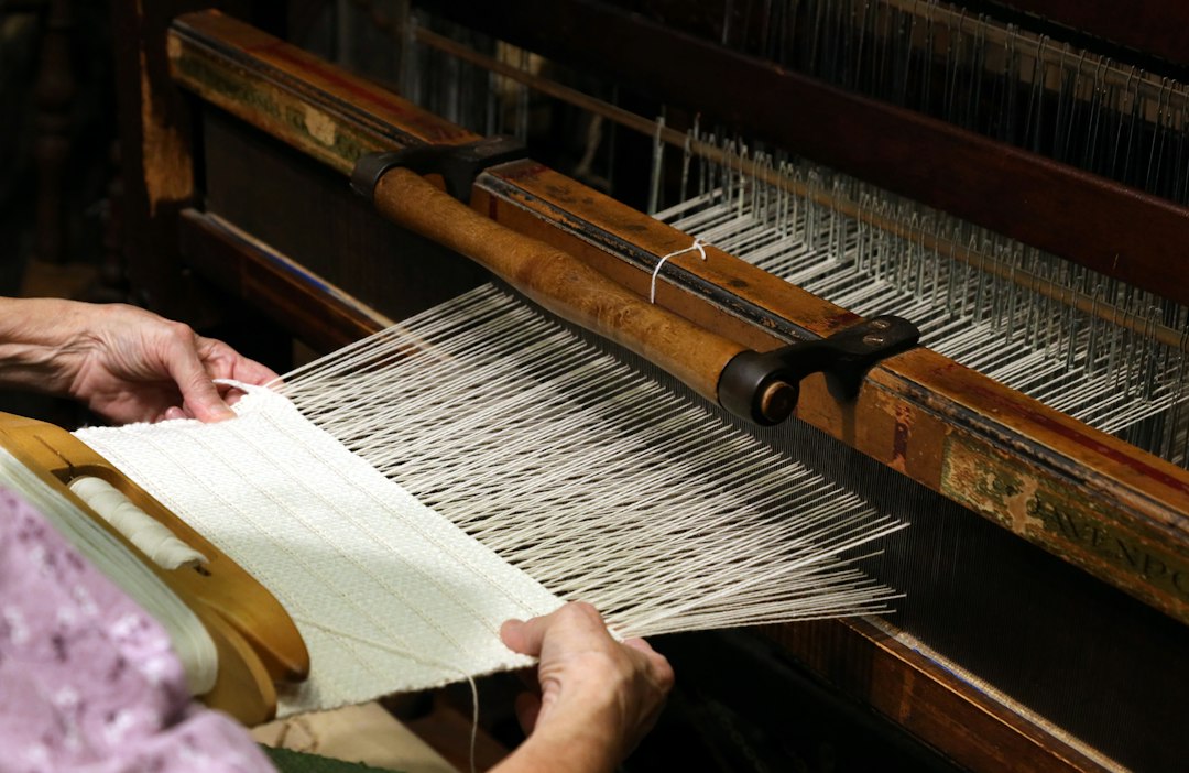 Mains d'une tisserande guidant le fil de coton sur un métier à tisser en bois traditionnel